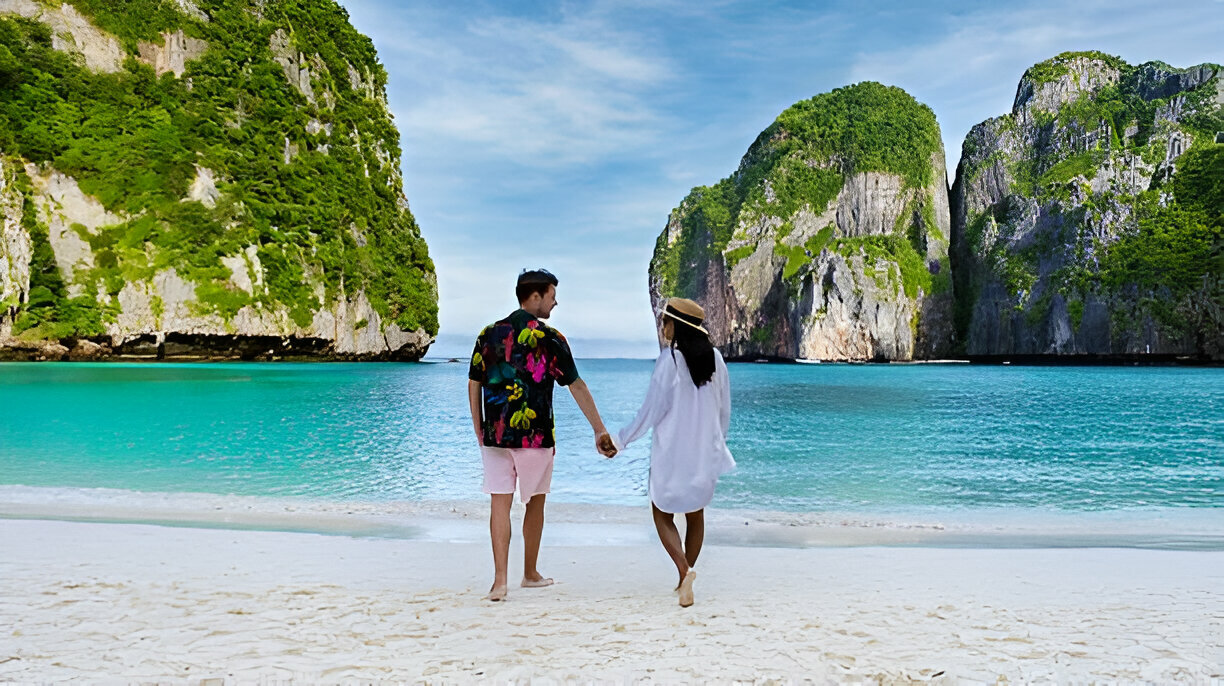 Couple walking hand-in-hand along the beach on Phi Phi Islands, Thailand, with stunning limestone cliffs and turquoise waters in the background—perfect for a romantic honeymoon getaway.